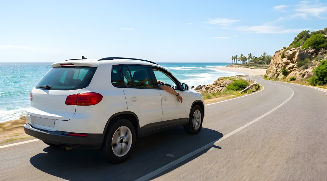 A white SUV driving along a sunny coastal road on the Gold Coast with the blue ocean in the background.