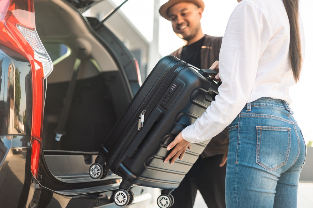 Happy couple puts his suitcase in the back of the car