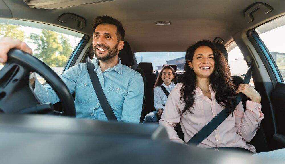 Happy-european-family-of-three-riding-car-traveling-by-automobile-together-parents-and-daughter-enjoying-road-trip-on-weekend