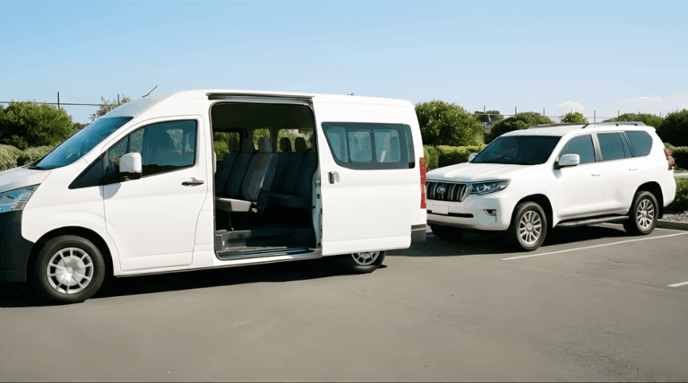 clean, white, unbranded 8-seater People Mover (Minivan style) parked next to a white SUV in a sunlit paved parking area. The side sliding door of the People Mover is open, revealing the spacious interior.
