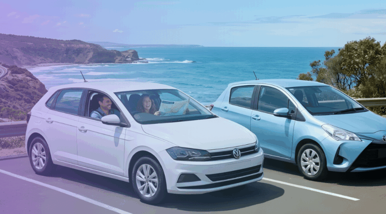 a compact white hatchback on the left and a slightly smaller economy light blue hatchback on the right—parked side-by-side on a smooth sealed asphalt surface overlooking a spectacular Australian coastal highway.