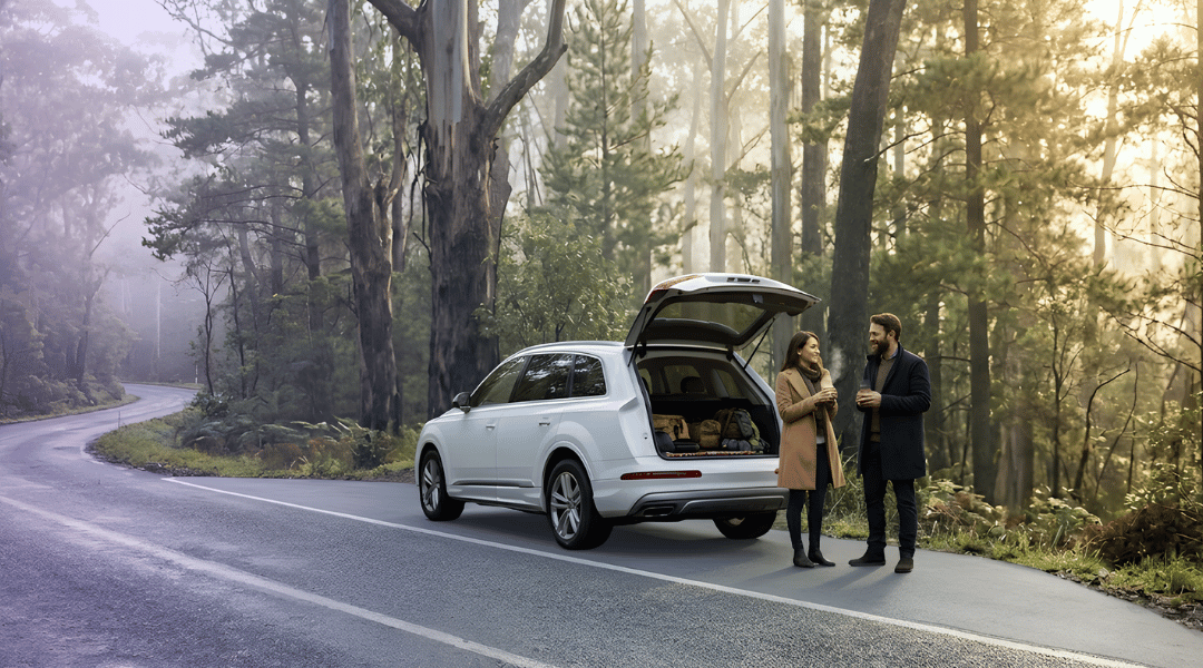 A sophisticated couple enjoying morning coffee beside their white rental SUV on a misty, pine-lined road in the Blue Mountains for Christmas in July.