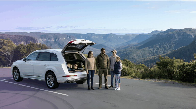 An Australian family enjoying a scenic valley view next to their pristine white SUV rental on a sealed mountain road.