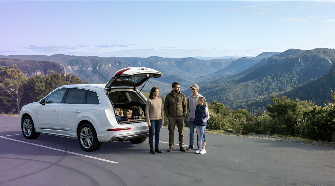 An Australian family enjoying a scenic valley view next to their pristine white SUV rental on a sealed mountain road.