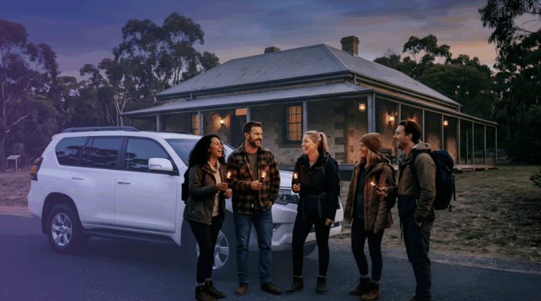 A group of friends laughing beside their white rental SUV as they arrive at a historic Australian building for a Halloween ghost tour.