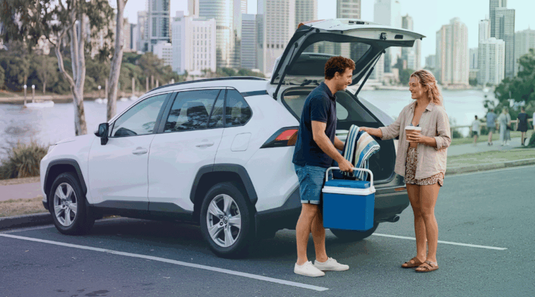 A smiling couple unloading beach gear from their white rental SUV near a quiet, secluded Gold Coast beach.