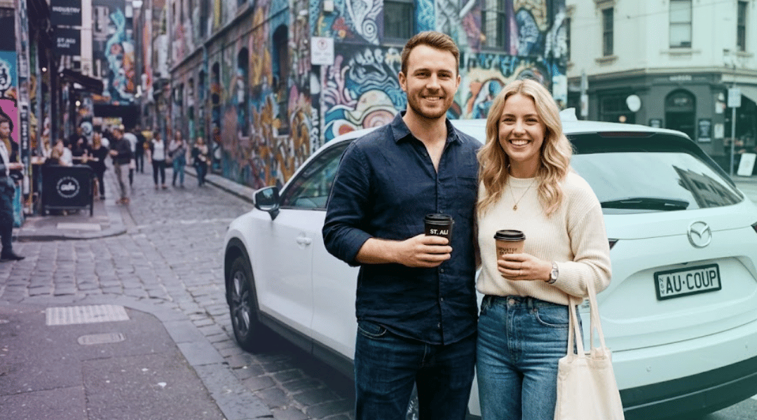 A smiling couple holding takeaway coffees next to their white rental SUV near a vibrant Melbourne lane-way.