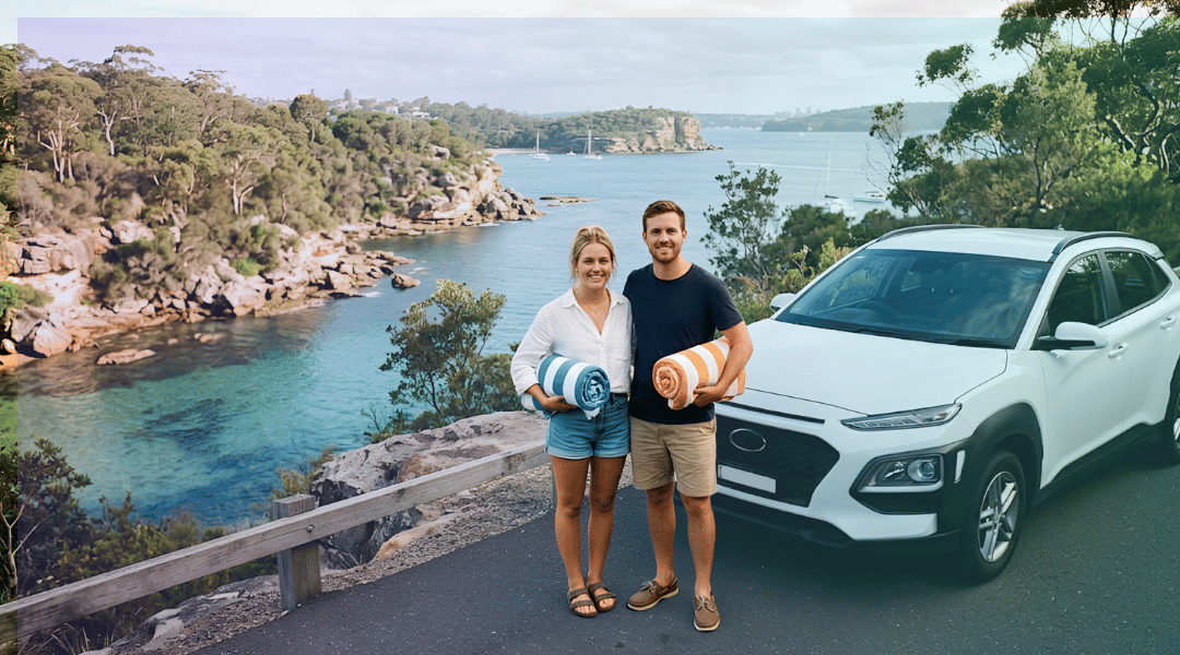 A smiling couple holding beach towels next to their white rental SUV near a secluded Sydney harbour cove.