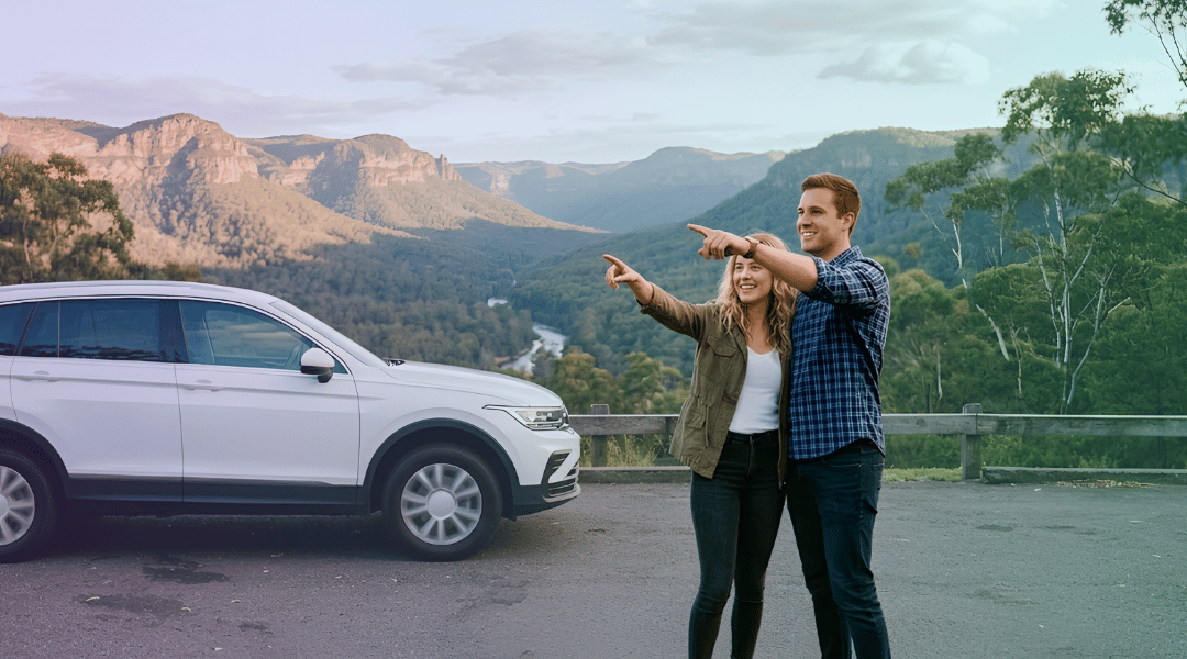 A couple admiring the sweeping mountain views next to their white rental SUV in the Scenic Rim.