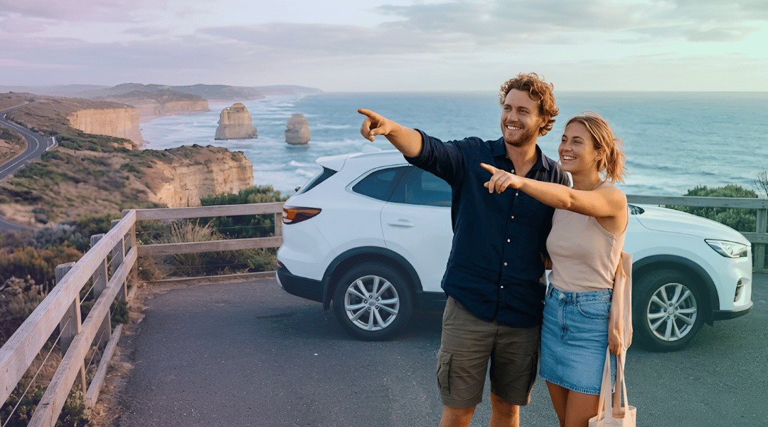 A smiling couple admiring the spectacular coastal views next to their white rental SUV along the Great Ocean Road.