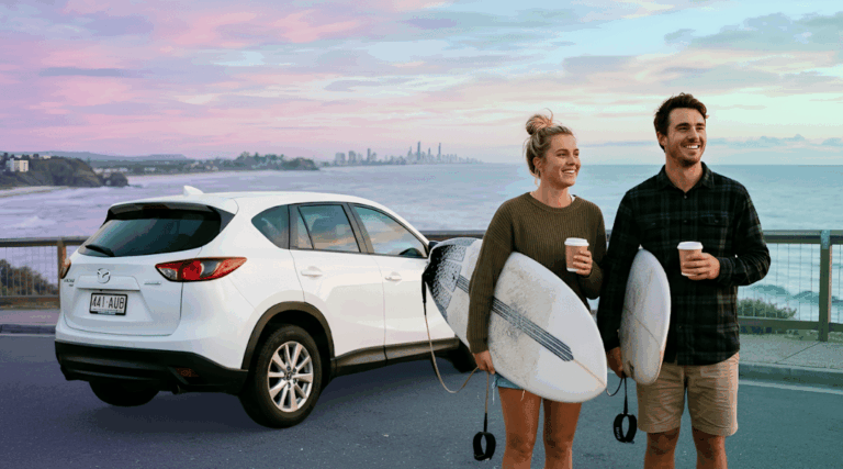 A smiling couple with coffees and a surfboard ready for a sunrise session next to their white rental SUV on the southern Gold Coast.