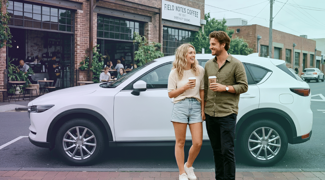 A smiling couple holding takeaway coffees next to their white rental SUV outside an artisanal Melbourne cafe.