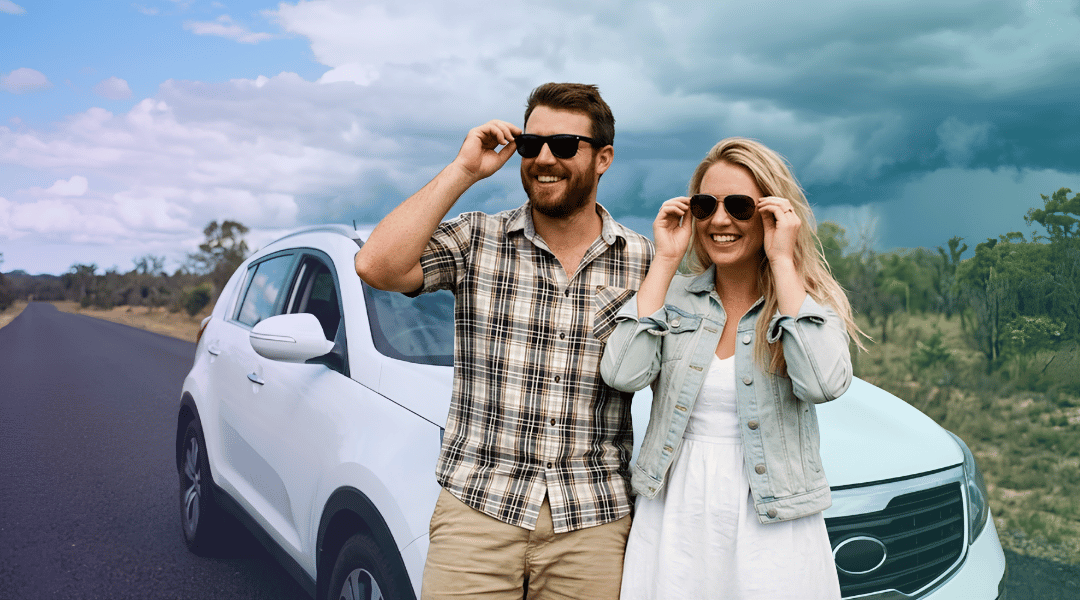 A smiling couple putting on sunglasses next to their white rental SUV, completely prepared for the Queensland weather.