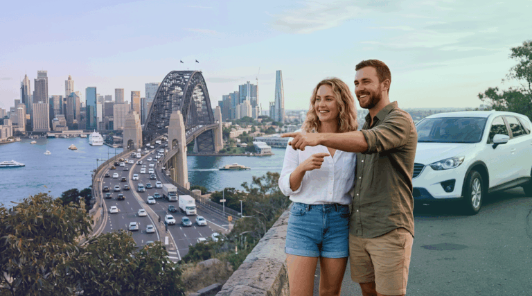 A smiling couple relaxed next to their white rental SUV overlooking the Sydney city skyline and flowing traffic.